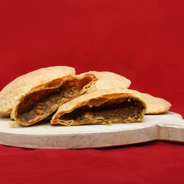 Several Caribbean Delight patties, one cut open to reveal a savory filling, on a white board.