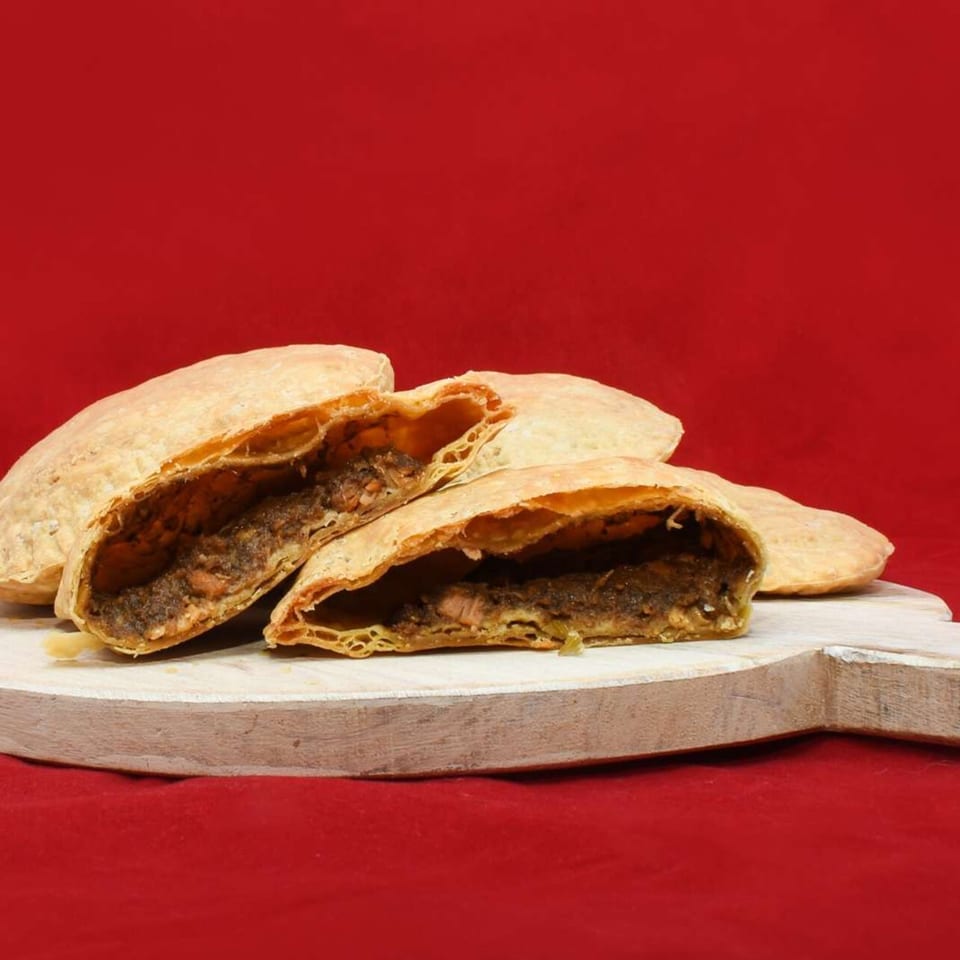 Several Caribbean Delight patties, one cut open to reveal a savory filling, on a white board.
