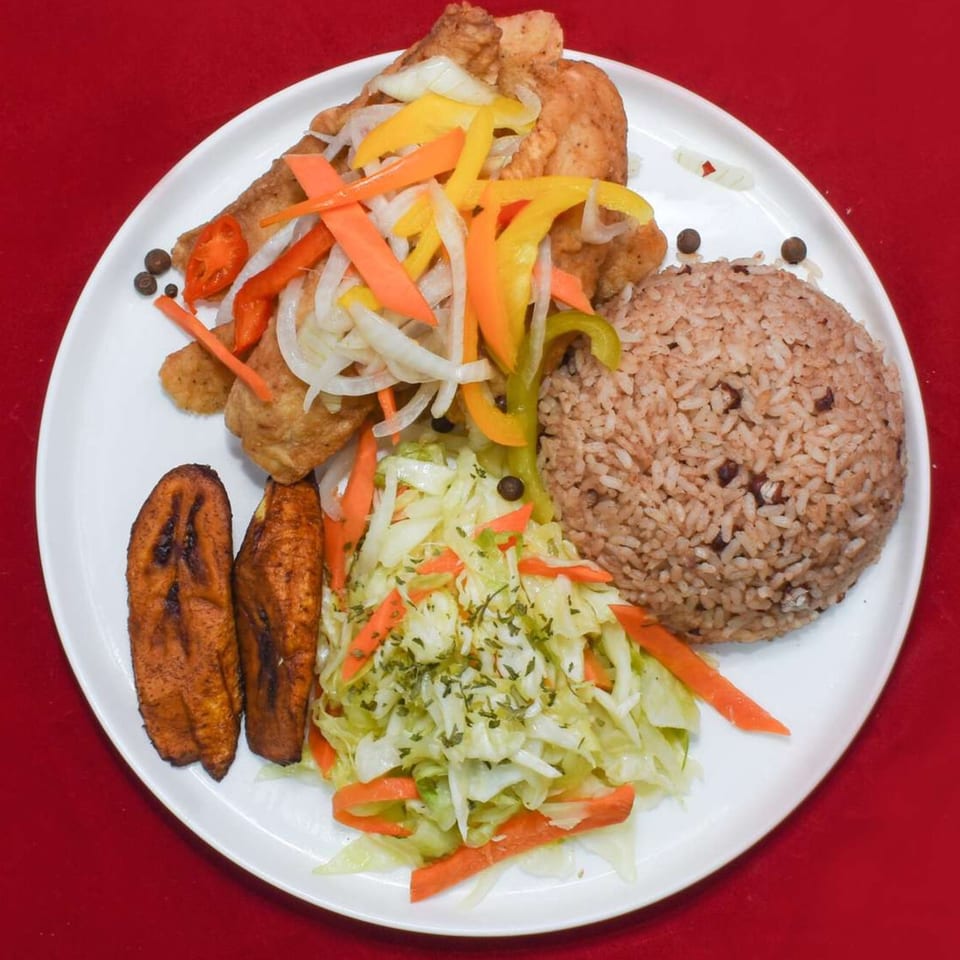 Caribbean Delight's fried chicken with rice and peas, plantains, and cabbage on a white plate.