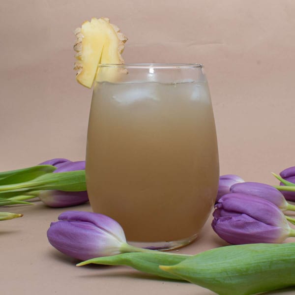 Iced Caribbean ginger beer with a ginger slice garnish, surrounded by purple tulips.