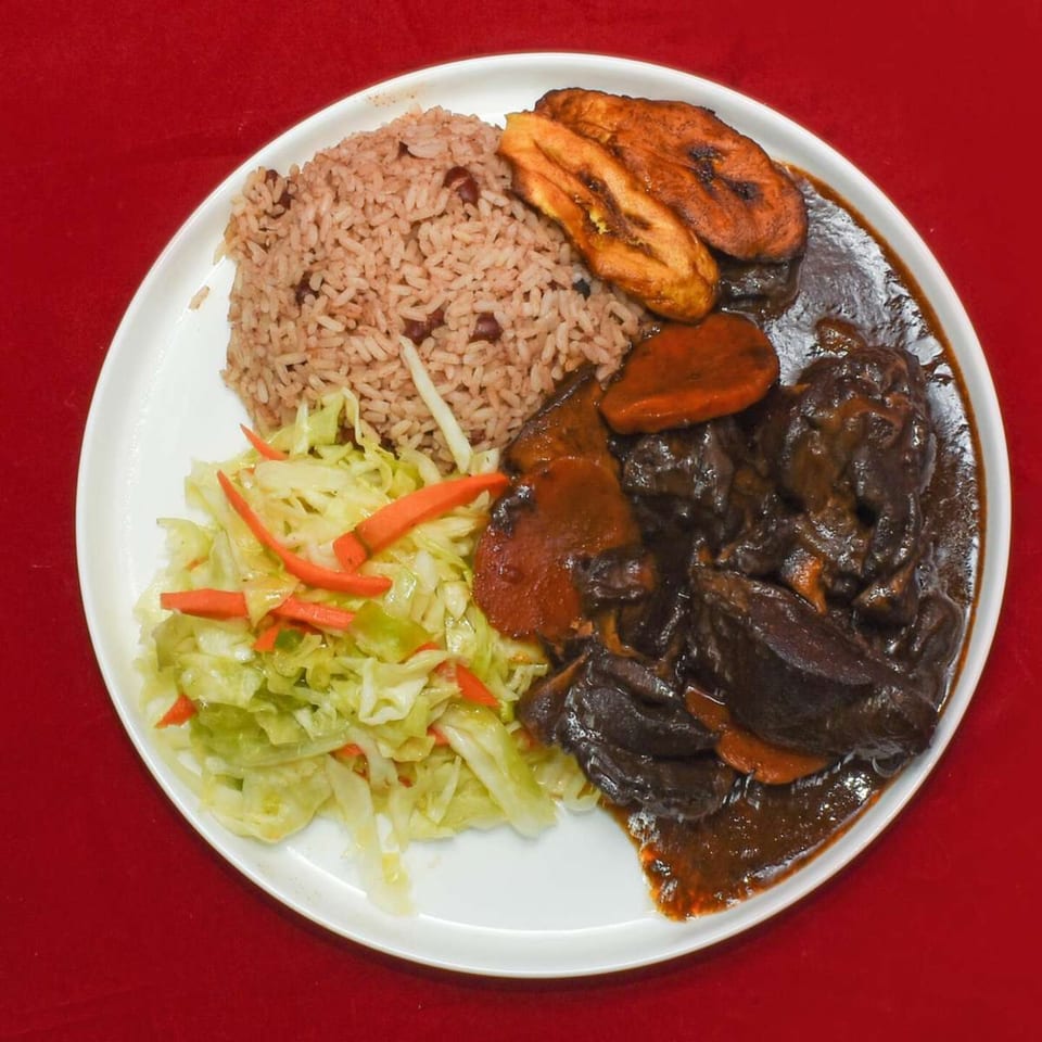A Caribbean Delight plate with rice and peas, stewed meat, fried plantains, and sautéed cabbage.