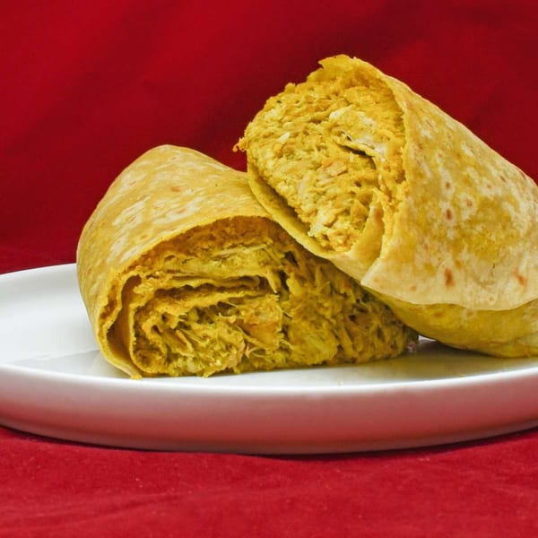 Two Caribbean Delight chicken roti wraps, filled with seasoned shredded chicken, on a white plate.