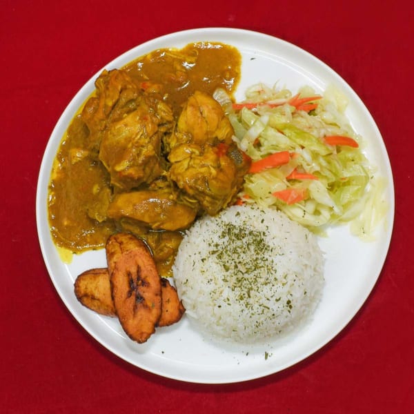 Curry chicken with rice, fried plantains, and cabbage salad on a white plate.